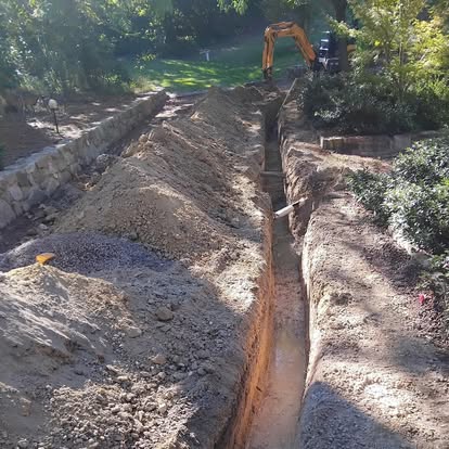 Excavator digging a trench beneath a stone driveway for new electrical services